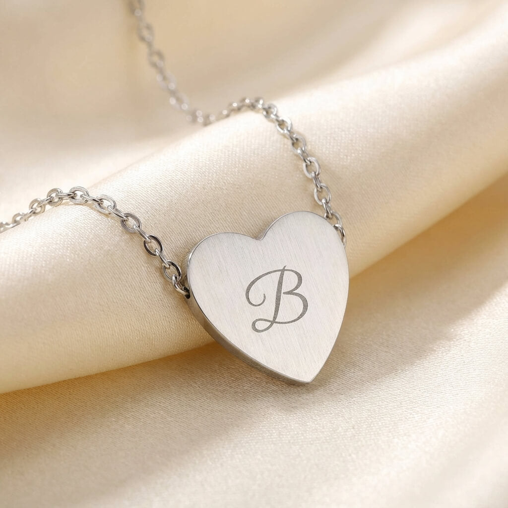 Silver heart-shaped necklace with engraved letter 'B' on a beige fabric background