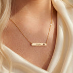 Gold necklace with 'Cooper' and paw print on a person wearing a white garment.