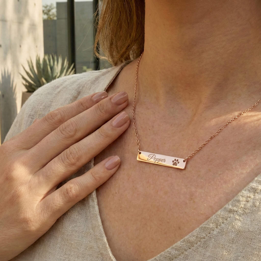 Person wearing a rose gold necklace with an engraved name and paw print design.