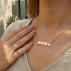 Person wearing a rose gold necklace with an engraved name and paw print design.
