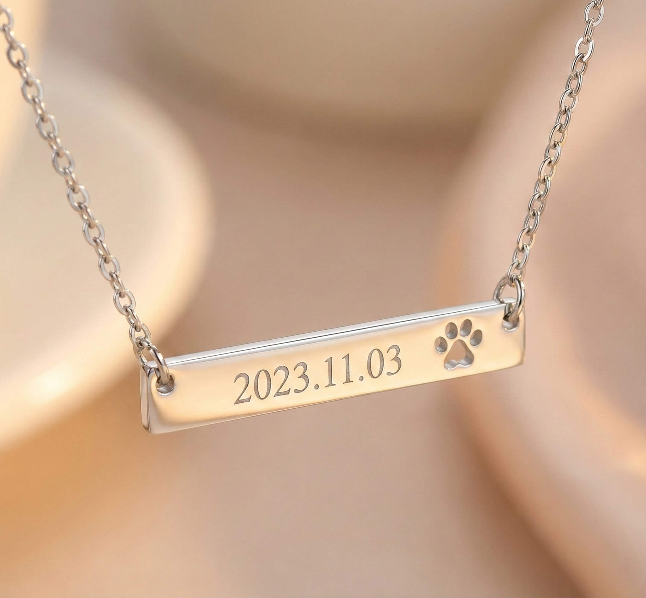 Gold necklace with a bar pendant featuring a paw print and engraved date on a beige background